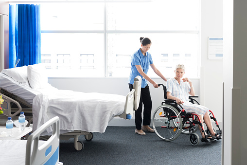 female patient in wheelchair on hospital ward. Disabled patient receiving help from female nurse.