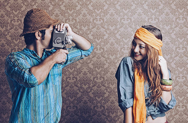 Young man filming his girlfriend in front of wallpaper background