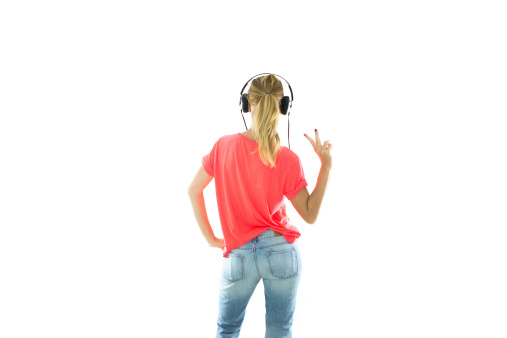Young woman from back view listening to music wearing headphones and making peace sign with fingers.