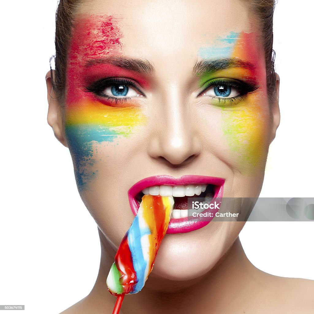 Fantasy Makeup. Painted Face. Lollipop Beautiful young woman with fantasy makeup eating a colorful lollipop looking at camera. Beauty and makeup concept. Closeup portrait isolated on white. Candy Stock Photo
