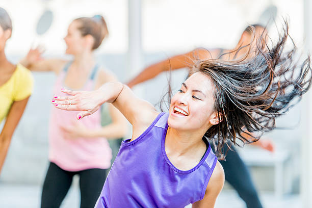 A multi-ethnic group of young adults are dancing together at a fitness class in the gym.