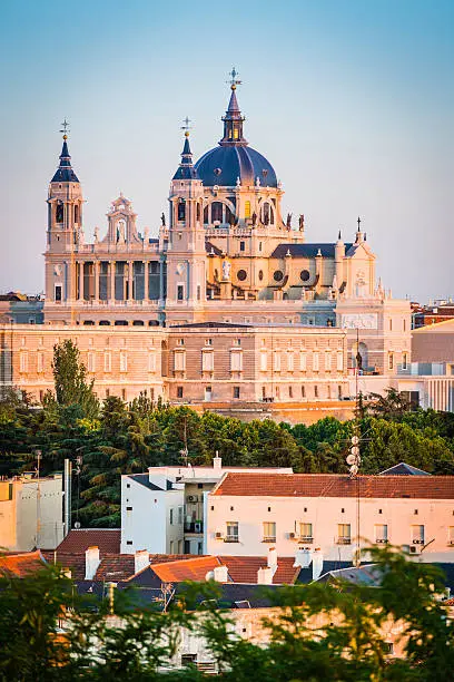 Warm dusk light illuminating the ornate domes and spires of the Almundena Cathedral and classical facade of the Palacio Real across the rooftops of central Madrid, Spain's vibrant capital city. ProPhoto RGB profile for maximum color fidelity and gamut.