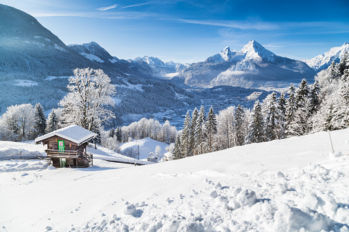 Panoramic view of beautiful winter wonderland mountain scenery in the Alps with traditional mountain chalet on a cold sunny day with blue sky and clouds