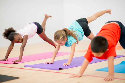 A multi-ethnic group of elementary age children are doing yoga together in the gym.