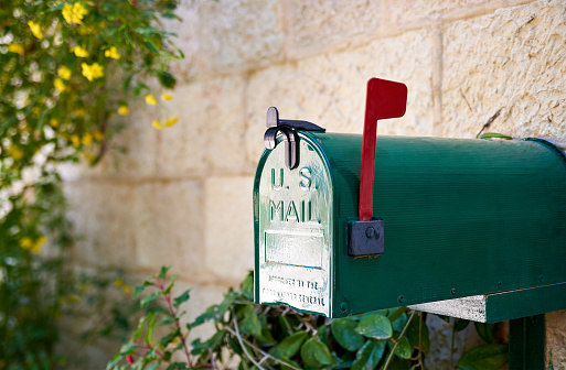 A woman is collecting post at home in autumn, Quebec, Canada. She is smiling and unlocking the mailbox. She is pickup-up her mail and looking at the letters she received.