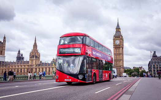 London, UK - July 8, 2015: Double-decker and the Big Ben in London. The bus is driving across the Westminster bridge with people walking in the background.