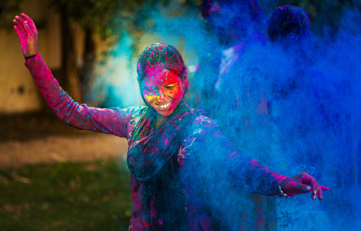 Young woman dancing around a cloud of color powder while celebrating the indian Holi day