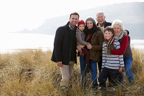 Multi Generation Family In Sand Dunes On Winter Beach Multi Generation Family In Sand Dunes On Winter Beach Smiling To Camera multi generation family photos stock pictures, royalty-free photos & images
