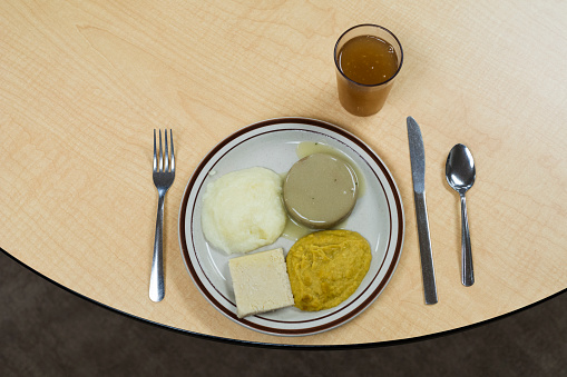 Plate of pureed food with blended chicken and gravy, corn, mashed potatoes and bread for patients with oral or pharyngeal dysphagia who have difficulty chewing regular foods; and nectar thickened tea for safer swallowing  served at lunch on a wooden table with silverware