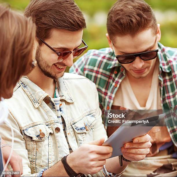 Young Men Friends Using Tablet Computer In Park Stock Photo - Download Image Now - Adult, Adults Only, Beautiful People