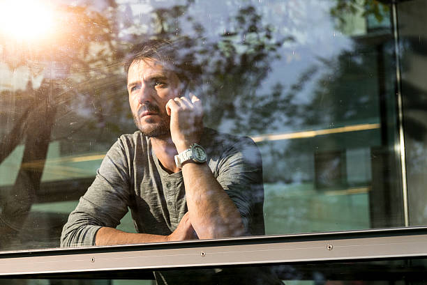 istock mature man standing behind window with mobile phone 503734024