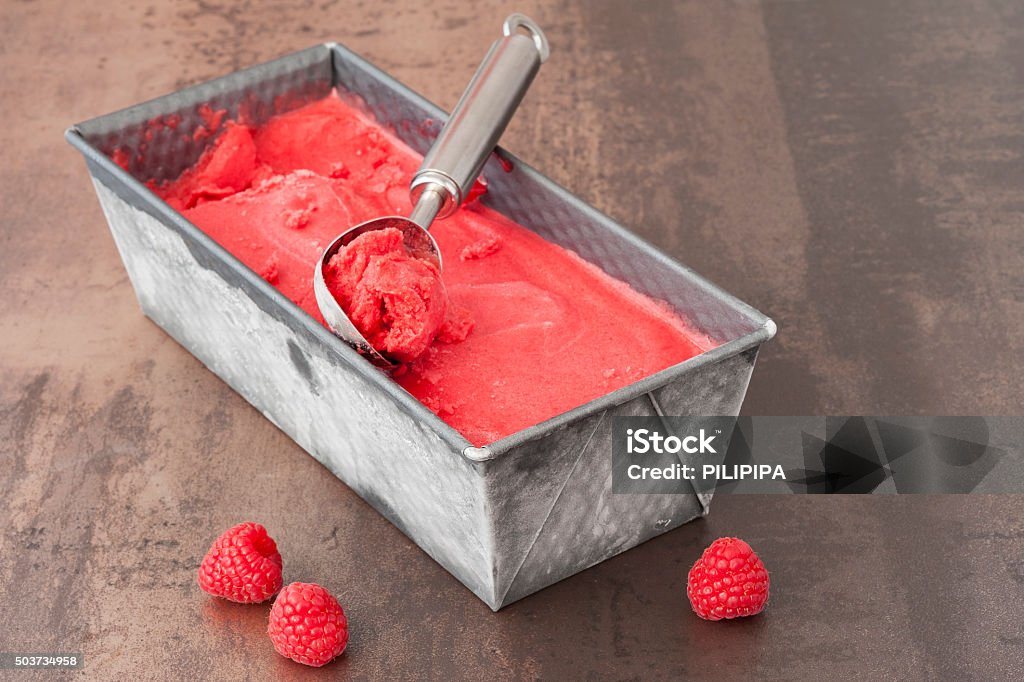 Raspberry Sorbet Fresh raspberry sorbet ice cream in a baking tin with a serving scoop on top. In the front are fresh raspberries Cold Temperature Stock Photo