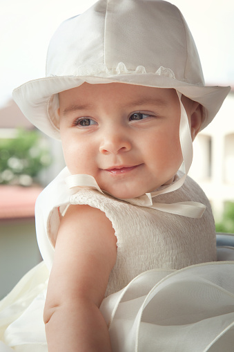Portrait of a child a few months with white dress and hat on the day of her baptism.
