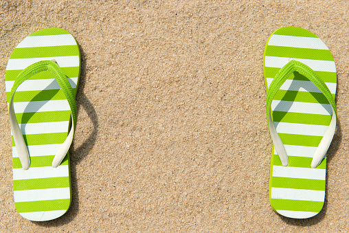 Pair of green striped flipflop on beach with copy space