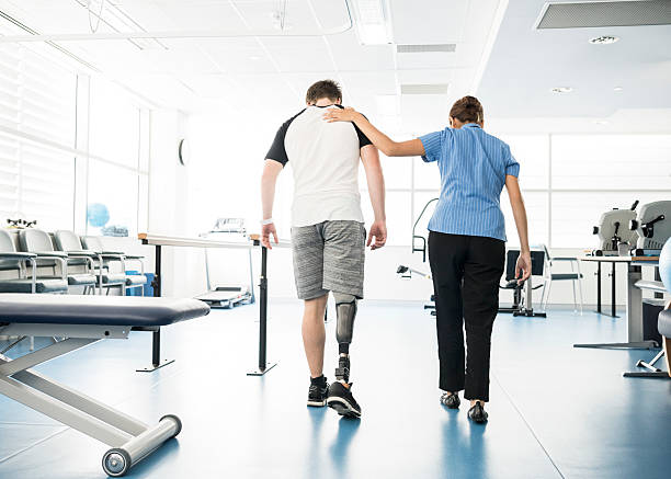 Physiotherapist helping young man with prosthetic leg Young man walking with prosthetic limb being assisted by female nurse in hospital. Woman with hand on patient's shoulder. hand on shoulder photos stock pictures, royalty-free photos & images