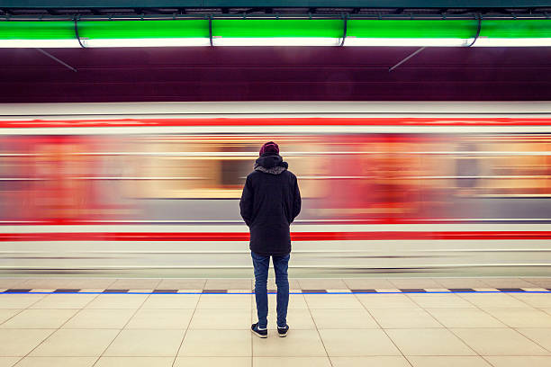 Man at subway station and moving train Lonely young man shot from behind at subway station with blurry moving train in background subway platform stock pictures, royalty-free photos & images