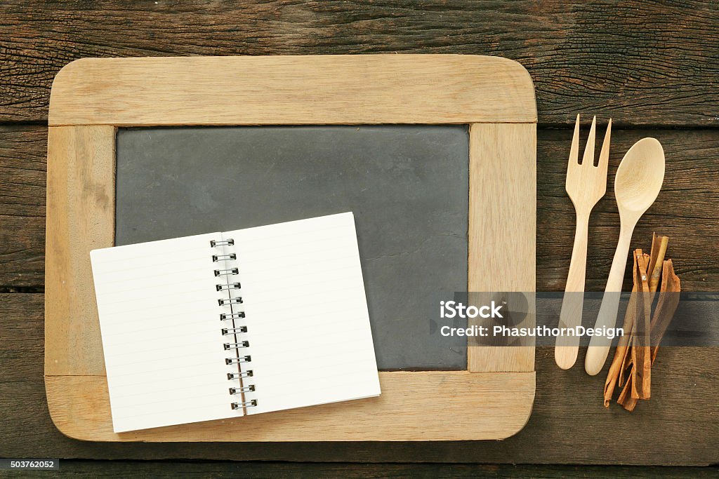 Slate chalkboard and wooden spoon and blank note book The slate chalkboard and wooden spoon and blank earth tone note book with cinnamon on the old dark brown wooden planks. Antique Stock Photo