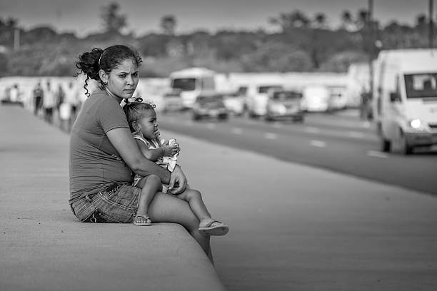 Havana, Cuba - November 6, 2015: Mother and child sitting on  the wall at Malecon in Havana, Cuba. This is a famous downtown shore line, lined up with great architecture from past now mostly run down after years being exposed to elements from Caribbean sea. Popular place for people of Havana to hang around, be in love, play music and fish. A must see location when visiting this great city. November, late afternoon in winter, people sitting on the wall near water.