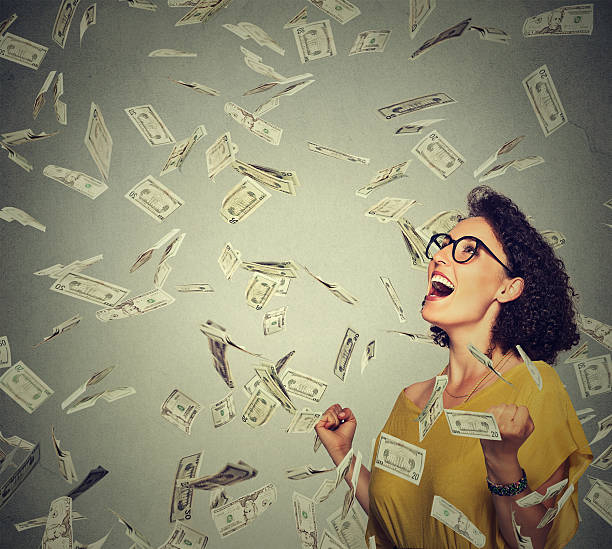 happy woman pumping fists celebrates success under money rain Portrait happy woman in glasses exults pumping fists ecstatic celebrates success under a money rain falling down dollar bills banknotes isolated on gray wall background with copy space free bingo stock pictures, royalty-free photos & images