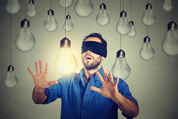 Blindfolded young man walking through lightbulbs searching for bright idea