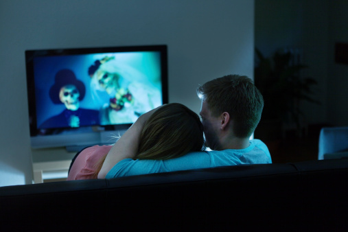 Couple watching Scary Halloween horror movie on TV together at home.