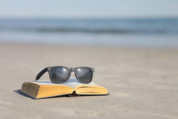 istock Sunglasses and book on the sand by the ocean 503785921