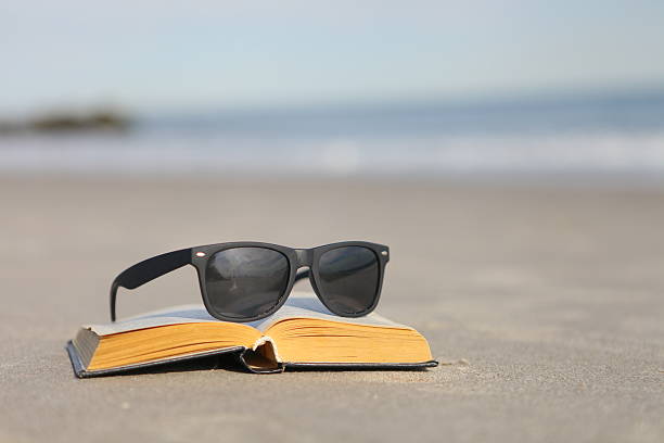 istock Glasses and a book on the sand by the ocean 503786331