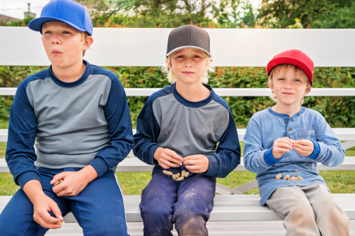 Three young brothers eating peanuts watching baseball game outdoors. Horizontal.
