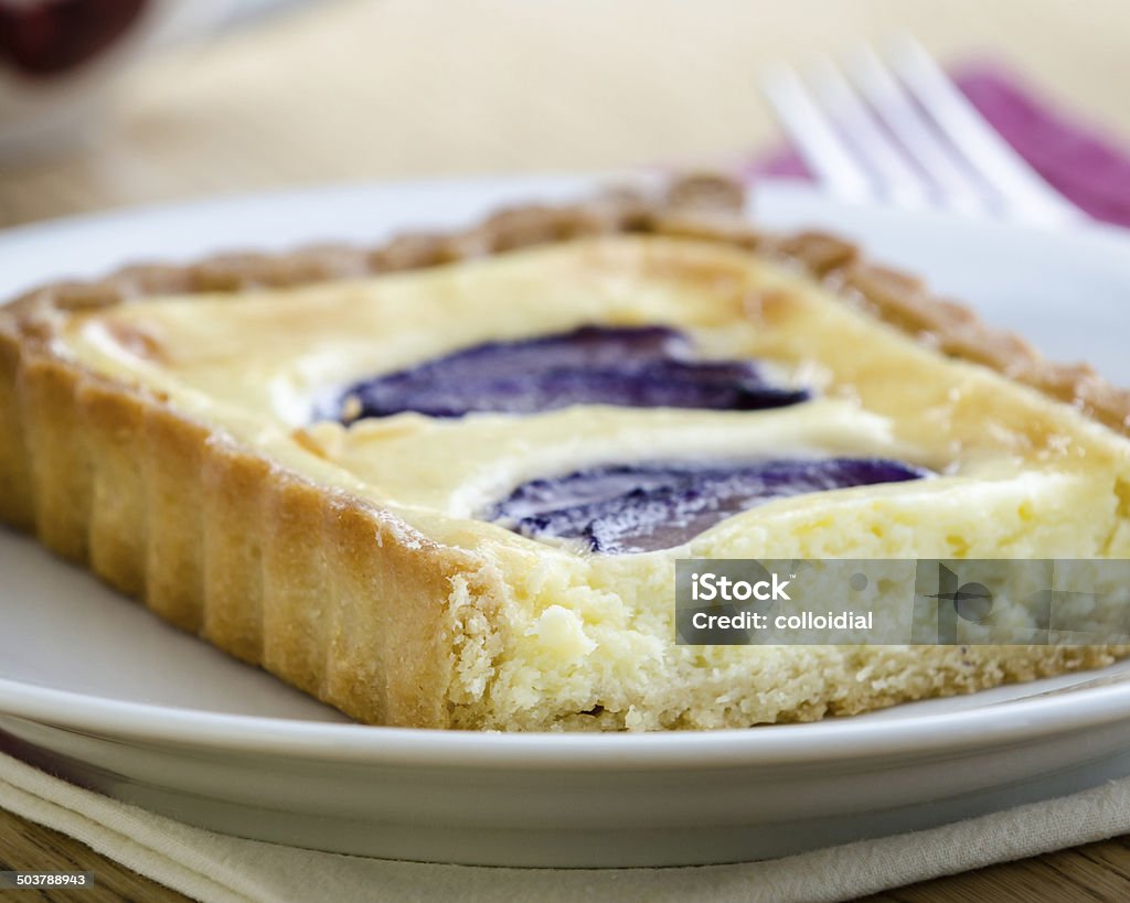 Plum Tart Fresh plum tart on a white plate, fork and cup in the background on light wood tabletop. Baked Stock Photo