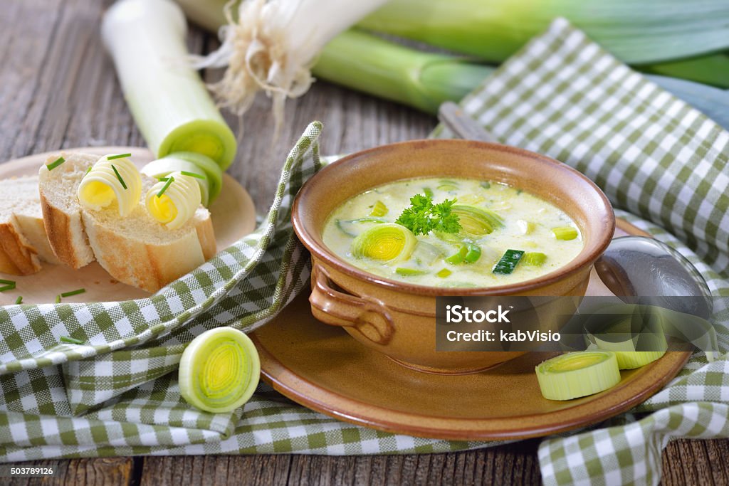 Cheese and leek soup Creamy vegetarian cheese and leek soup with buttered baguette, served on a wooden table Leek Soup Stock Photo