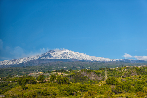 Green landscape and snowy volcano Etna against blue sky, Sicily, Italy