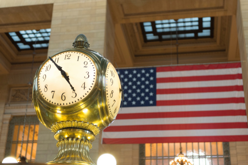 Manhattan, NY - July 18, 2014: The clock inside Grand Central Terminal with the american flag in the background located in New York City. The clock was created by  Seth Thomas company in 1913, the time piece is one of the masterpieces of the station.