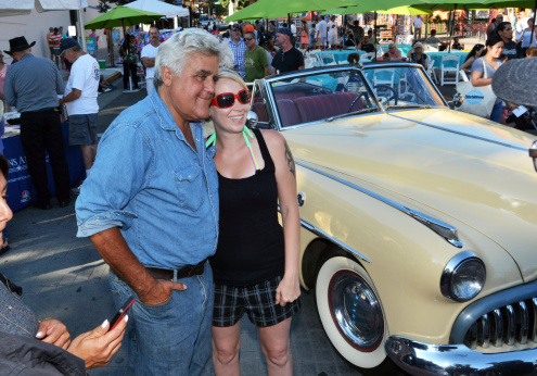 Burbank, CA, USA – July 26, 2014: Former Tonight Show host Jay Leno with his arm around a fan poses beside a classic automobile at the Downtown Burbank Car Classic auto show.