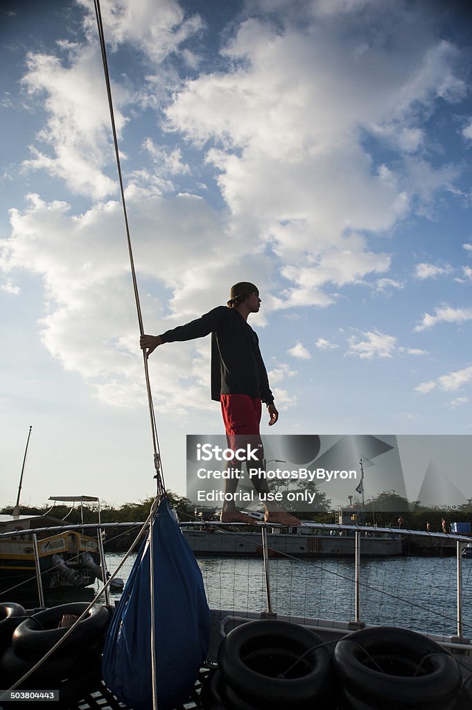 Young shipmate prepares to navigates boat departure from harbor Kona, Hawaii - September 1, 2013: A young male shipmate stands on the bow section of a boat preparing to set sail to navigate boat from the harbor in Kona, Hawaii. Adult Stock Photo