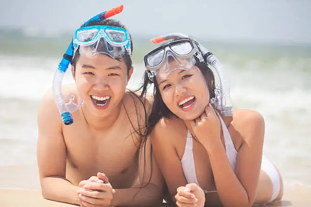 Young beautiful couple lying on the beach and smiling at camera