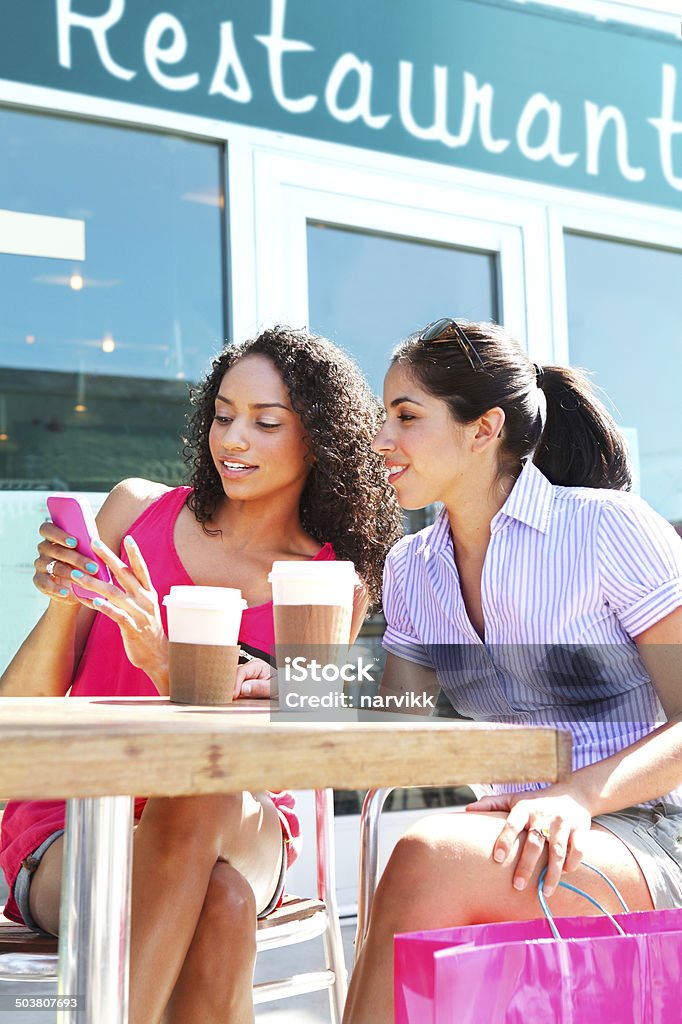 Girls having fun with smartphone in restaurant Girls having fun with smartphone after shopping in restaurant Adult Stock Photo