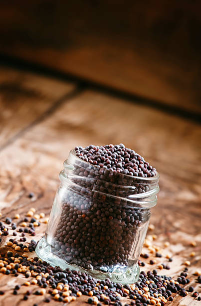 Black mustard seeds in a glass jar Black mustard seeds in a glass jar on the old wooden background, selective focus dijonnaise stock pictures, royalty-free photos & images