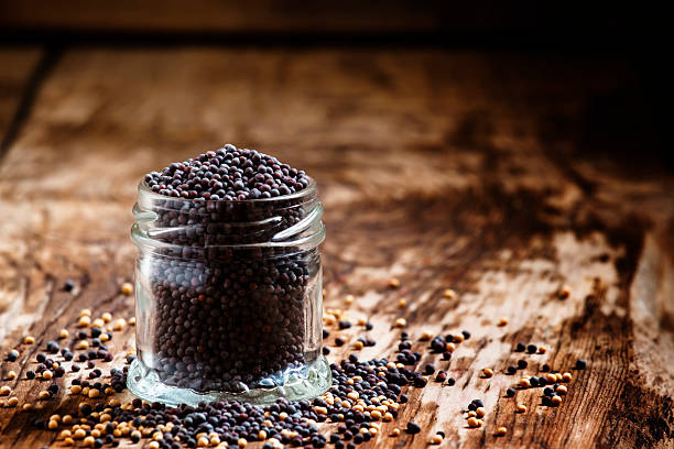 Black mustard seeds in a glass jar Black mustard seeds in a glass jar on the old wooden background, selective focus dijonnaise stock pictures, royalty-free photos & images