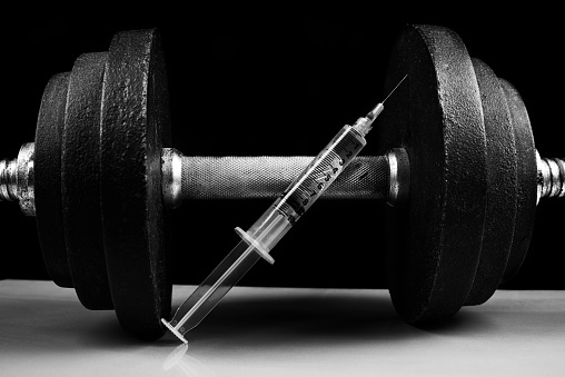 A dumbell with a syringe shot in studio as a concept for the illegal use of steroids or human growth hormone.