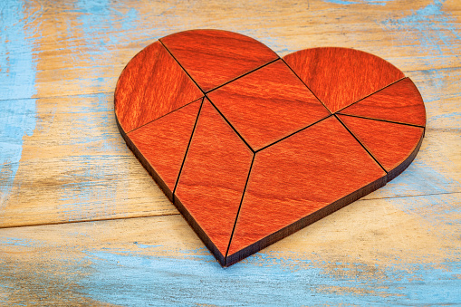 heart version of tangram, a traditional Chinese Puzzle Game made of different wood parts to build abstract figures from them, painted wood background