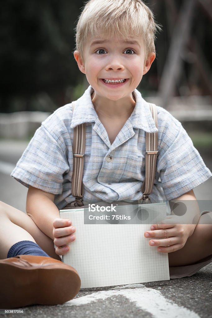 Retro School Boy and Notebook Young amazed school boy in retro clothing sitting at the ground and hold a small paper notebook in his hands (copy space) 2015 Stock Photo