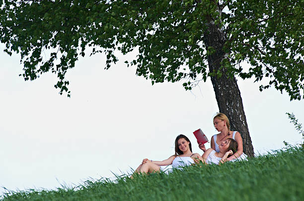 Mother and daughters reading the book under a tree