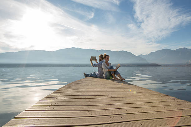 istock Young couple relax on lake pier with book,digital tablet 503861816