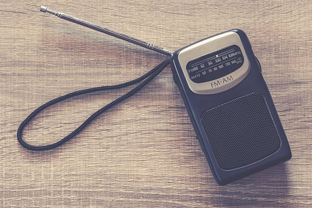 Old portable transistor radio Old portable transistor radio on a wooden table. Retro cross processed image vintage portable silver radio stock pictures, royalty-free photos & images
