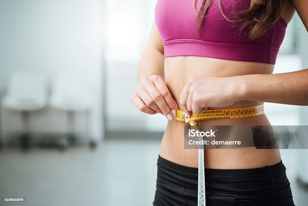 Slim woman measuring her thin waist Slim young woman measuring her thin waist with a tape measure, close up Dieting Stock Photo