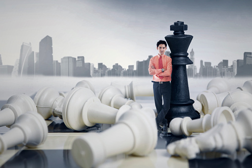 Smiling male entrepreneur winning chess game on city background