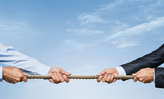 Two businessman pulling a rope in opposite directions over sky background with copy space