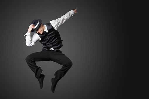 Young male professional dancer dancing in studio isolated on gray background.