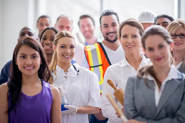 A multi-ethnic group of varied business professionals are standing tgoether and are smiling while looking at the camera.