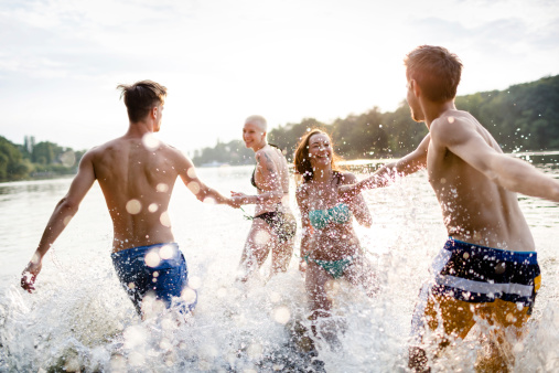 Two young couples having fun and running into a lake.